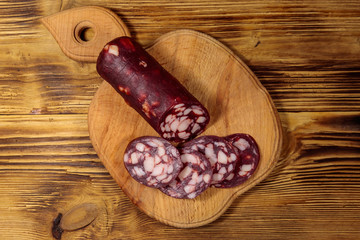 Sliced salami sausage on cutting board on wooden table. Top view