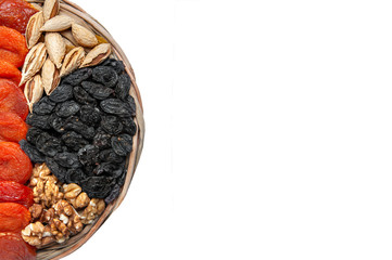 Many dried fruits on a round wooden plate, cashew nuts, prunes, figs, raisin and apricots isolated on white