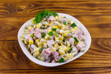 Tasty salad with sausage, green pea, canned corn, bell pepper, cucumber and mayonnaise on wooden table