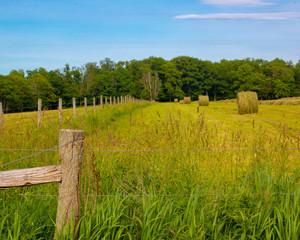 rural scene with fields, hay, bales, fence, sky, clouds, trees