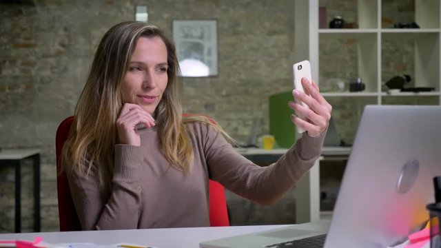 Closeup portrait of beautiful female office worker taking seductive selfies on her phone in the office