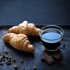 Fresh french croissants with cup of espresso and coffee beans on vintage dark background.