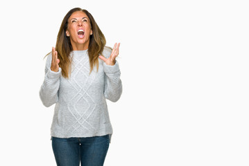 Beautiful middle age adult woman wearing winter sweater over isolated background crazy and mad shouting and yelling with aggressive expression and arms raised. Frustration concept.