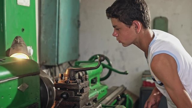 Teenage boy in tank top using industrial lathe