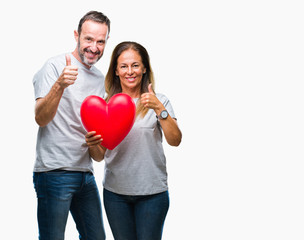 Fototapeta na wymiar Middle age hispanic casual couple in love holding red heart over isolated background happy with big smile doing ok sign, thumb up with fingers, excellent sign