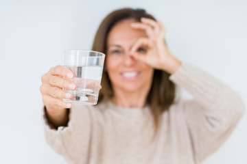 Middle age woman drinking glass of water isolated background with happy face smiling doing ok sign with hand on eye looking through fingers