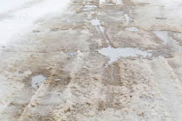 road is paved with cracks in pits and puddles from the snow. Landscape of the winter road in cloudy gray weather.