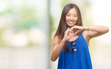 Young asian woman over isolated background smiling in love showing heart symbol and shape with hands. Romantic concept.