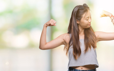 Young asian woman wearing sunglasses over isolated background showing arms muscles smiling proud. Fitness concept.