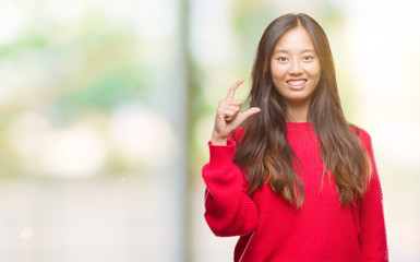 Young asian woman wearing winter sweater over isolated background smiling and confident gesturing with hand doing size sign with fingers while looking and the camera. Measure concept.