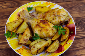 Baked chicken drumsticks with potatoes in a plate on wooden table