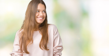 Young beautiful brunette woman wearing pink sweatshirt over isolated background looking away to side with smile on face, natural expression. Laughing confident.