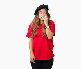 Young beautiful brunette fashion woman wearing red t-shirt and black beret over isolated background looking stressed and nervous with hands on mouth biting nails. Anxiety problem.