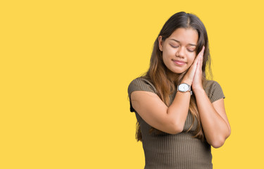 Young beautiful brunette woman over isolated background sleeping tired dreaming and posing with hands together while smiling with closed eyes.