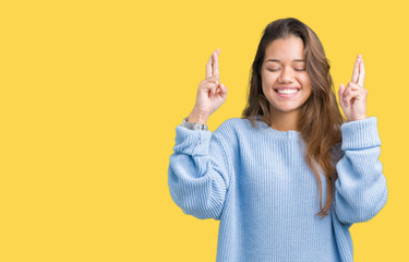 Young beautiful brunette woman wearing blue winter sweater over isolated background smiling crossing fingers with hope and eyes closed. Luck and superstitious concept.