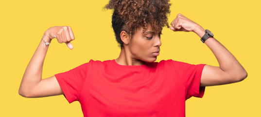 Beautiful young african american woman over isolated background showing arms muscles smiling proud. Fitness concept.