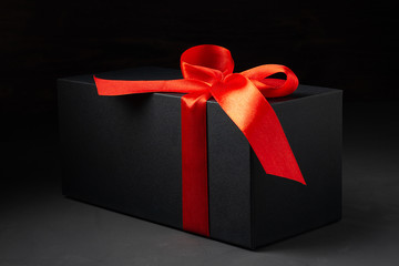 Black gift box with red ribbon on dark background