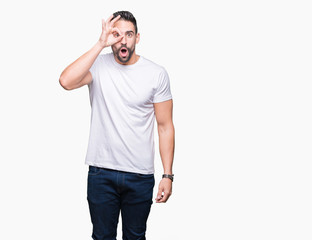 Young man wearing casual white t-shirt over isolated background doing ok gesture shocked with surprised face, eye looking through fingers. Unbelieving expression.