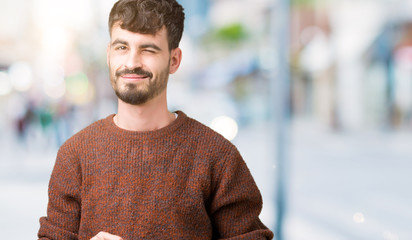 Young handsome man wearing winter sweater over isolated background winking looking at the camera with sexy expression, cheerful and happy face.