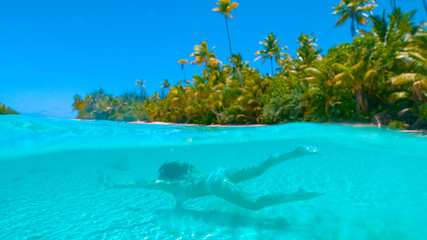 HALF UNDERWATER: Carefree girl on holiday swimming in the glassy ocean water.