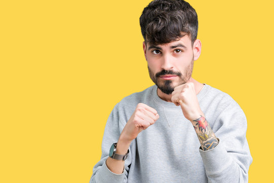 Young handsome man wearing sweatshirt over isolated background Ready to fight with fist defense gesture, angry and upset face, afraid of problem