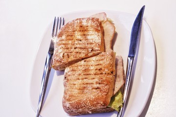 Delicious hot sandwich with turkey, tomatoes, salad. in a plate with cutlery on the table.