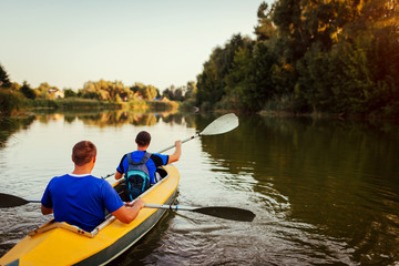 Young men rowing kayak on river at sunset. Couple of friends having fun canoeing in summer