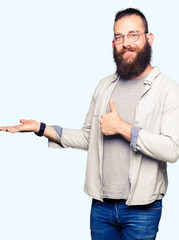 Young blond man wearing glasses Showing palm hand and doing ok gesture with thumbs up, smiling happy and cheerful