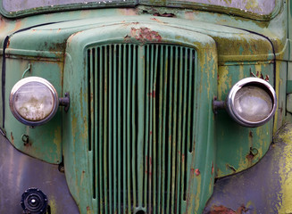 close up of the front of an old abandoned rusting green 1940s truck covered in moss