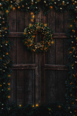 Old wooden door decorated with Christmas garland and wreath, and with warm glowing fairy lights