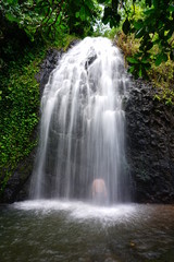Obraz premium View of the silhouette of a man bathing under a cascading waterfall in Tahiti, French Polynesia
