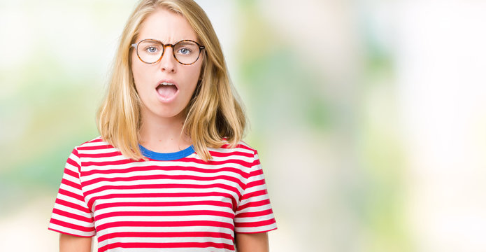Beautiful young woman wearing glasses over isolated background In shock face, looking skeptical and sarcastic, surprised with open mouth