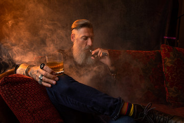 Portrait eines attraktiven Geschäftsmannes mit einerE- Zigarre und einem Glas Whiskey vor dunklem...