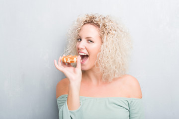 Young blonde woman over grunge grey background eating belgian waffle with a confident expression on...