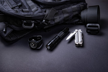 Everyday carry (EDC) items for men in black color - backpack, tactical belt, flashlight,  watch and silver multi tool.  - obrazy, fototapety, plakaty