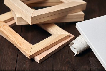 Wooden stretcher bars and a rolled canvas lying on a dark brown background, timber, subframes
