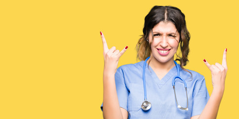 Young adult doctor woman wearing medical uniform shouting with crazy expression doing rock symbol...