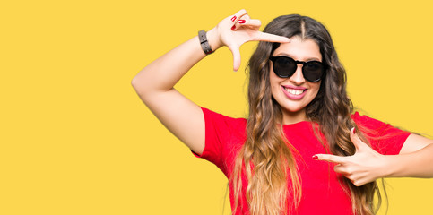 Young beautiful woman wearing red t-shirt and sunglasses smiling making frame with hands and fingers with happy face. Creativity and photography concept.
