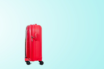 A red travel suitcase on wheels, isolated on a green pastel background. Travel concept, packing up before departure. Preparing for travel, going on vacation, break, rest.