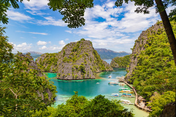 Elevated view of lagoon with boats surrounded by rocks and turquoise sea. Coron. Palawan, Philippines.