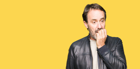 Middle age handsome man wearing black leather jacket looking stressed and nervous with hands on mouth biting nails. Anxiety problem.