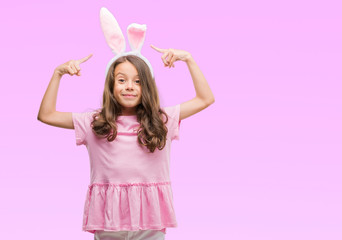Brunette hispanic girl wearing easter rabbit ears very happy pointing with hand and finger
