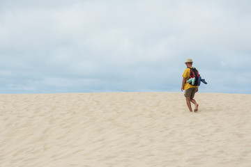 young man with backpack going in the sandy desert