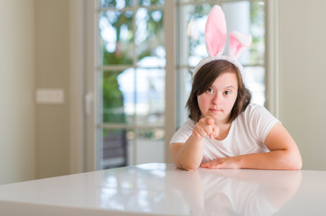 Down syndrome woman at home wearing easter rabbit ears pointing with finger to the camera and to you, hand sign, positive and confident gesture from the front