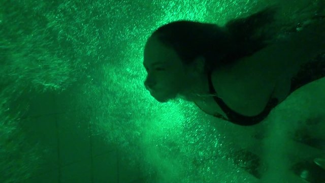 Cute girl diving underwater through bubbles in green light in aquapark.