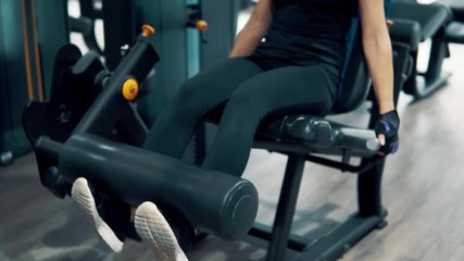 Young fit woman doing leg exercise using training machine in gym. View from forward. 4k shot