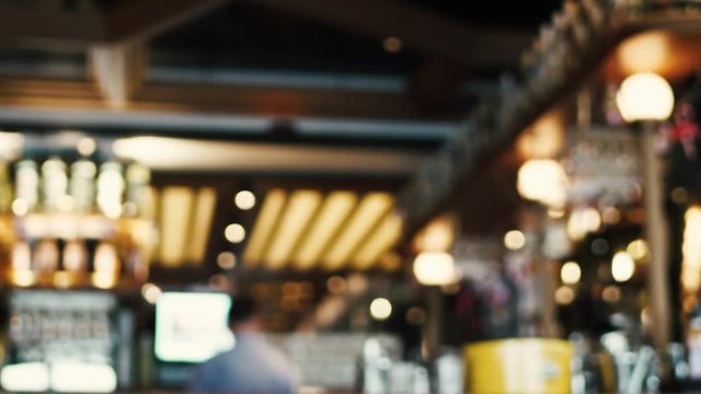 Blurred image of the interior of a large beautiful restaurant with bright lighting. The waitress comes to the working bar and the bartender, gives visitors a menu and goes for a drink. Defocused staff