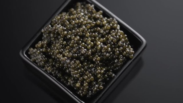 Black Caviar closeup. Natural sturgeon black caviar in square dish rotated on black background, rotation. Delicatessen. Slow motion. 3840X2160 4K UHD video footage