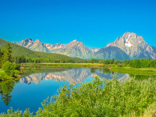 Teton Range of the Rocky Mountains reflecting in the calm waters of Jackson Lake at Grand Teton National Park, Wyoming, United States. North America in summer season, blue sky, copy space.