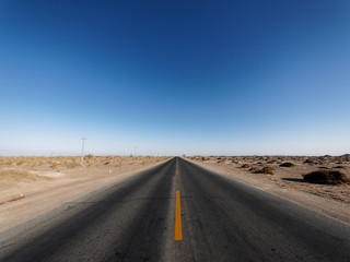 Centered view of an endless asphalt road in desert, low angle straight rough road with blue sky background, magic world.